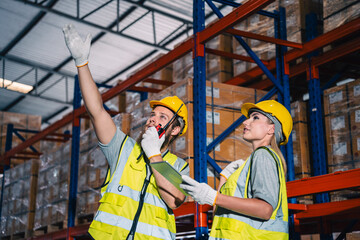 Warehouse worker logistic team wearing hard hat working in aisle between tall racks with packed goods warehouse for industry business of import, export delivery to global market, shipping management