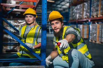 Warehouse worker logistic team wearing hard hat working in aisle between tall racks with packed...