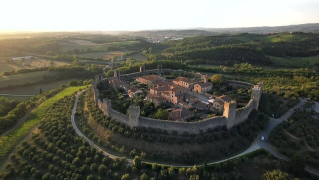 4K aerial drone shot of Monteriggioni, Tuscany, Italy, at sunset, golden hour, medieval town used in Assassin's Creed II, surrounded by lush green valleys