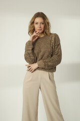 Fashion portrait of young woman in brown winter sweater and beige wide pants on the white background	
