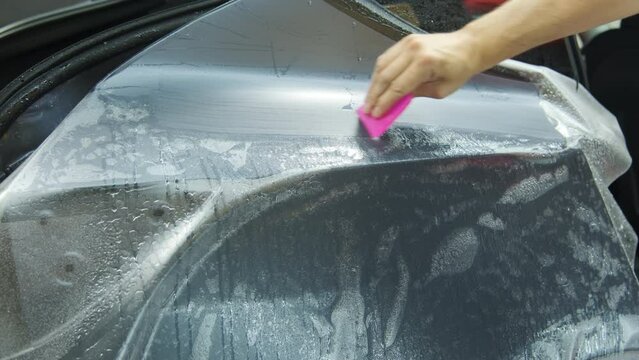Process of applying a protective PPF film to a car. Closeup view of Hands of a professional applying a protective film. Closeup footage