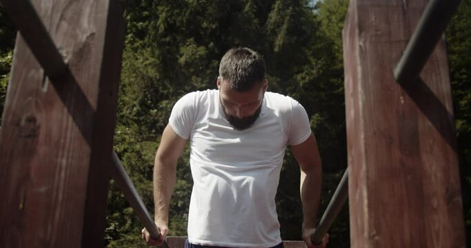 Portrait of a young man athlete while doing push-ups on parallel bars.