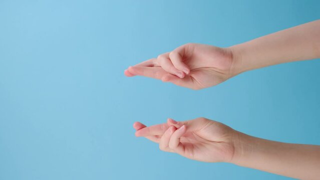 Vertical footage of female hands praying with crossed fingers hopes for miracle good outcome, isolated on blue background with copy space. Body language concept. Advertising area, workspace mock up