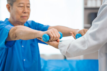 Asian people mature woman doctor giving male elderly patient through indoor physical therapy in a healthcare wheelchair, emphasizing hands-on support and recovery. expert physical therapy