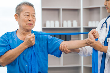 Obraz premium Asian people mature woman doctor giving male elderly patient through indoor physical therapy in a healthcare wheelchair, emphasizing hands-on support and recovery. expert physical therapy