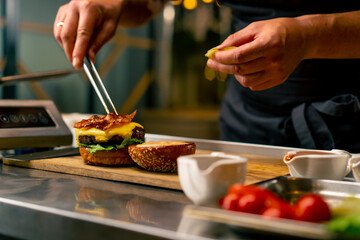 A close-up of a chef preparing a burger with beef patty with vegetables and cheese in the professional kitchen of an Italian restaurant