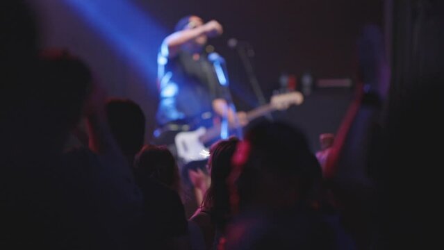 A rock band performs in a nightclub - a man plays a guitar and the crowd looks at him