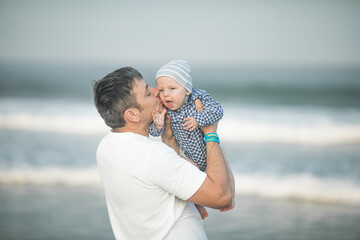 Cheerful young  father with  his  infant son having fun together by seaside, dad throwing up kid in the air