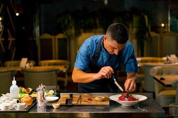 Fototapeta na wymiar The chef of an Italian restaurant decorates a dish he has prepared in a professional kitchen 
