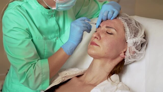 Cosmetologist makes injections in skin of beautiful girl. Anti aging dermatology procedure. Female enjoying facial treatment, moisturizing and rejuvenating medical procedures