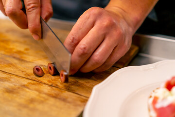Obraz na płótnie Canvas Close-up of a chef cutting olives with a knife while preparing a salad in the kitchen of an Italian restaurant