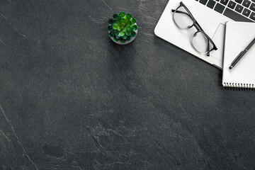 Obraz premium Top view of laptop, glasses and notepad on dark textured background.