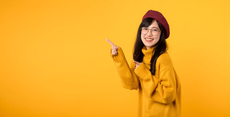 Look. Young pretty asian woman wearing yellow sweater and red beret expression pointing finger to free copy space for showing product isolated on yellow background. Education advertisement concept