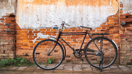 Fototapeta na wymiar Vintage bicycle on old rustic dirty wall house, many stain on wood wall. Classic bike old bicycle on decay brick wall retro style. Cement loft partition and window background.