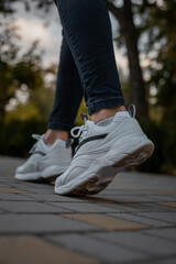 White sneakers on the feet of a girl in black jeans on the street
