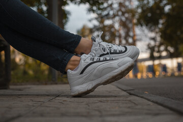 White sneakers on the feet of a girl in black jeans on the street