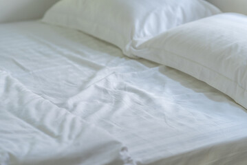 Soft pillows and white towel on clean white bed. Pillows bed with bedding sheets in bedroom. Bed sheets and pillows messed. Hotel, resort or home can relax on bed for deep sleep.