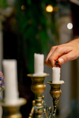 A close-up of a hand that uses a lighter to light candles standing in a candlestick on a table in an Italian restaurant
