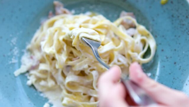 Piatto di deliziosi spaghetti alla carbonara, una tipica ricetta di pasta condita con una salsa a base di uova, pecorino e guanciale, cibo italiano. incompetent girl wraps spaghetti on a fork