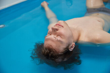 Handsome young man is swimming in the pool on his back. Relaxation and spa therapy.