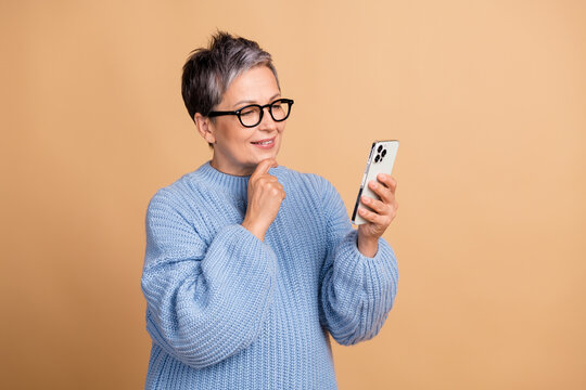 Portrait of minded creative lady hand touch chin use samrt phone empty space isolated on beige color background