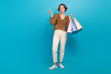 Full body portrait of pretty positive lady hold mall bags indicate finger empty space isolated on...