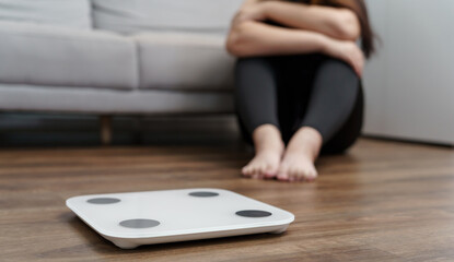 Fototapeta premium Sad woman with fat upset bored of dieting Weight loss fail&nbsp; Fat diet and scale sad asian woman on weight scale at home weight control