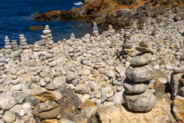 Fototapeta na wymiar Pebbles monticules in the Papoa island in the site of geological interest of the cliffs of the Peniche peninsula, portugal, in a sunny day with the rock formations.