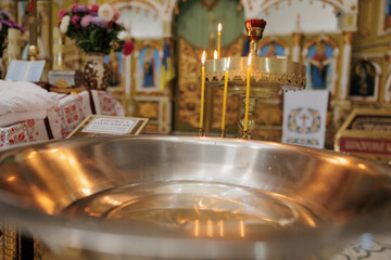 Baptismal font with blessing water and wax candles for Newborns baptism rite in Orthodox church. - obrazy, fototapety, plakaty