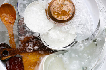 Dishes with bowls and wooden spoon in water and bubbles of dishwashing liquid