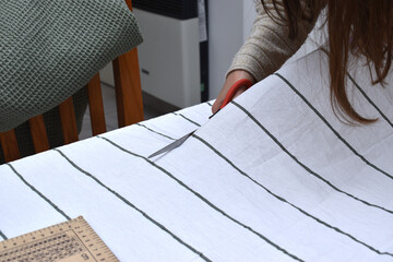 woman measuring and cutting a white fabric with stripes for textile work
