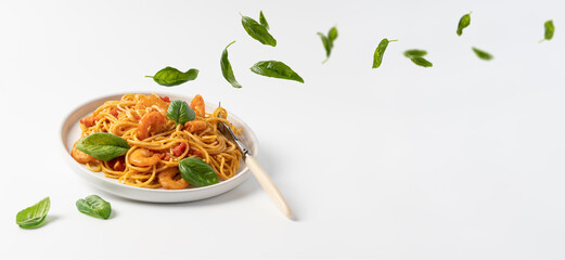 Shrimp pasta marinara paste levitating on white background with basil leaves falling in plate. Seafood spaghetti, Mediterranean cuisine