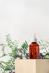 Cosmetic serum on wooden cube on white background with flowering plants. Natural organic beauty products