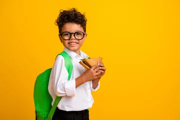 Fotobehang Profile photo of little boy carry rucksach hands hold sandwich empty space isolated on yellow color background © deagreez