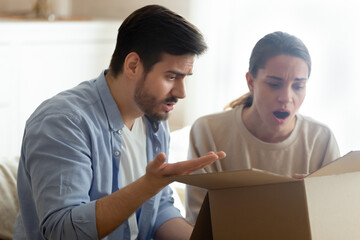 Fototapeta premium Angry man and woman annoyed by bad delivery service, unboxing parcel, looking into open cardboard box, dissatisfied customers received wrong or broken internet store order, complaint