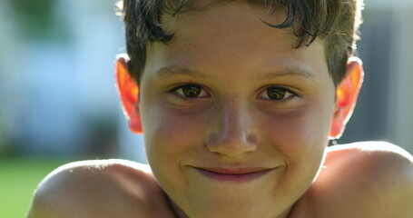 Handsome young boy child face smiling feeling happy and joy in outdoor sunlight. Kid portrait real life smile