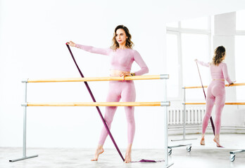 Slim ballerina woman girl in pink tracksuit. Stretching at ballet machine with resistance rubber. Athletic flexibility.Dancer trains in dance hall.Fitness club sports training workout,yoga instructor