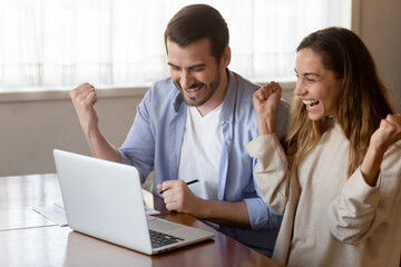 Overjoyed young couple celebrating success, looking at laptop screen, happy man and woman reading...