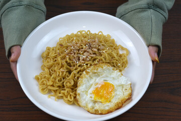 top view of woman hands showing or presenting plate of fried noodle with egg on the wood table