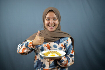 excited and smiled asian hijab woman enjoy fried noodles with egg. happy eating lunch concept with thumbs up