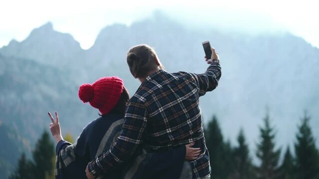 Young man and woman making selfie using smartphone on the mountain forest nature background. Couple in love dating outdoor. Two people hug and care each other. Romantic travel holiday vacation