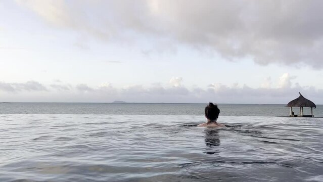Woman swimming in an infinity pool in Mauritius overlooking the ocean. Luxury vacation experience with tropical scenery, relaxation and an exclusive island lifestyle.