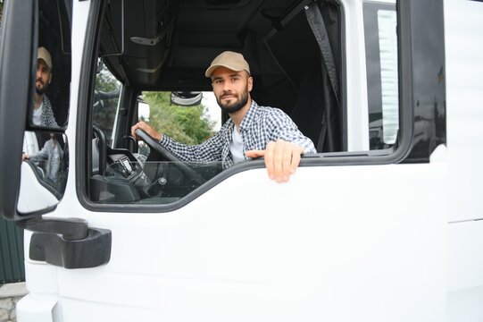 A driver sitting inside the semi-truck while looking through the open window with multiple trucks parked in the background