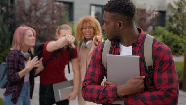 Sad upset offended victim boy student guy African American suffering man bullied of group multiracial students teens classmates thumb down mocking bully abused bullying university college aggression