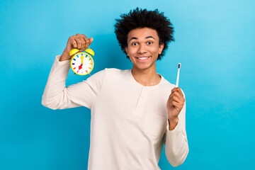 Portrait of funky handsome man toothy smile arm hold toothbrush bell ring clock isolated on blue color background