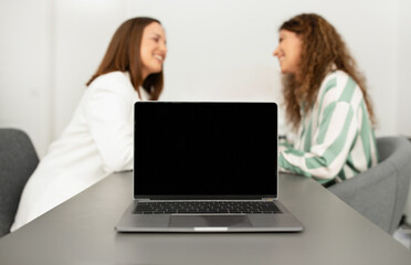 Laptop With Empty Screen On Table While Businesswomen Talking Indoor