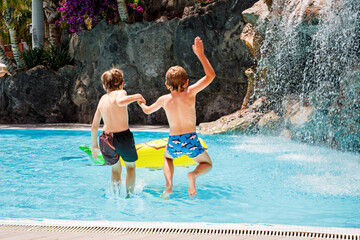 Two happy little kids boys jumping in the pool and having fun on family vacations in a hotel...
