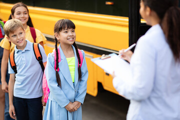 Black female teacher updating check list of children entering school bus