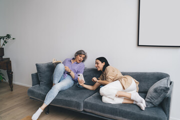 Happy mother and daughter watching smartphone together on sofa