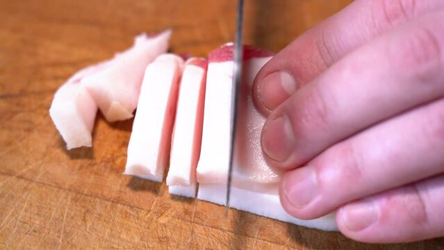 Slicing of salted pork fatback on cutting board, close-up. Ukrainian traditional food - salo